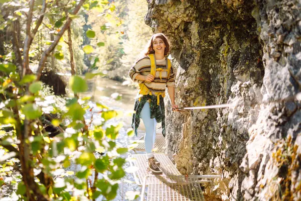 Sırt çantalı kadın yürüyüşçü dağlardaki yaya asma köprüsünde yürüyor. Genç bir kadın dağ manzarasından zevk alıyor ve açık havada özgürlüğü hissediyor. Seyahat, özgürlük kavramı.