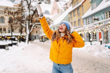 A happy woman with red lipstick has fun with the snow while walking along the snow-covered city streets. A beautiful tourist enjoys a sunny winter day. Concept: beauty, weekend, and lifestyle.