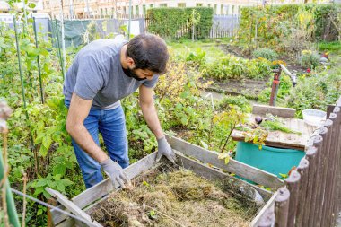 Genç sakallı Pakistanlı ya da Hintli erkek çiftçi, bahçesinde yemyeşil çimenler ve yapraklı çalılarla çevrili kuru yaprak ve otlardan gübre yapar.