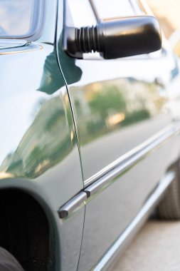 Pürüzsüz, siyah bir yan aynanın olduğu yeşil bir arabanın yakın çekim görüntüsü. Araç ayrıca otomotiv park lambası, lastik, kaput ve aydınlatma sistemini de gösteriyor.