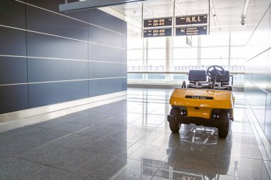 Çağdaş bir havaalanı terminalinde parlak döşemeleri ve aydınlatıcı işaretleri olan sarı bir elektrikli araba var.