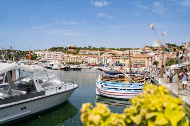 Güneşli bir gökyüzünün altındaki canlı binaların yakınındaki bir limanda renkli tekneler güzel bir sahil manzarası yaratıyor.
