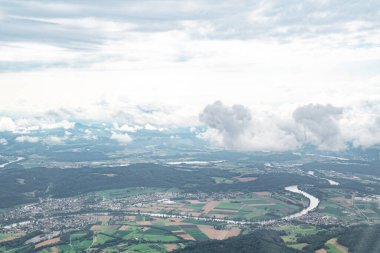 Hava perspektifi, dalgalı nehirleri, kabarık bulutları ve parlak mavi gökyüzü olan sakin bir kırsal bölgeyi gösteriyor.