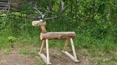 Ormanın arka planında çimlerin üzerinde duran gerçek boynuzlu el yapımı ahşap geyik oyuncağı. Doğadan esinlenilmiş oyun, halk sanatı ve geleneksel zanaat kavramı