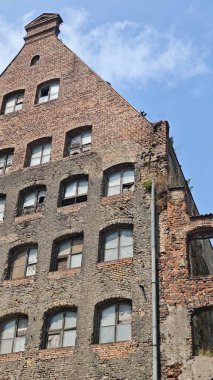Kırık camları ve mavi gökyüzünün altında yıpranmış yüzüyle terk edilmiş eski bir tuğla bina. Kentsel bozulma, zaman geçişi ve mimari bozulma kavramı