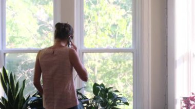 Evin penceresinin önünde akıllı telefonu olan genç bir kadının arka plan görüntüleri.