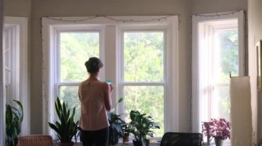 Evin penceresinin önünde akıllı telefonu olan genç bir kadının arka plan görüntüleri.