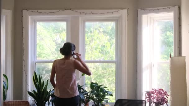 自宅の窓の前にスマートフォンを持つ若い女性のリアビュー映像 — ストック動画