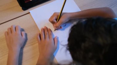 Çocuk masadaki tablet bilgisayarı kullanarak çizgi film karakteri çiziyor. 