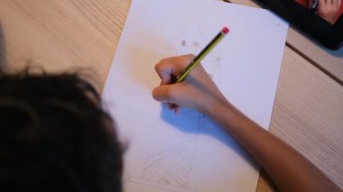 Çocuk masadaki tablet bilgisayarı kullanarak çizgi film karakteri çiziyor. 