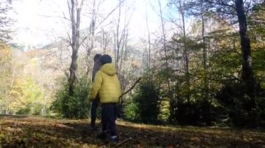 Oğullarıyla birlikte sonbahar ormanında yürüyen genç bir kadın.