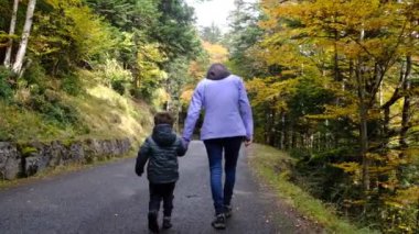 Anne oğluyla birlikte sonbahar parkında yürüyor.