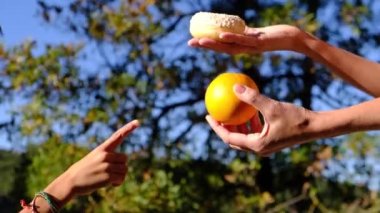 Anne ve oğlunun elleri meyve, endüstriyel hamur işi ve donut arasında seçim yapıyor. Sağlıklı meyve ve abur cubur arasında seçim yapmak zararlı beslenme, diyet konsepti yoluyla yararlı. Gıda eğitimi 