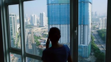 Pencerenin yanındaki telefonu kullanan kadın silueti