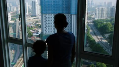Pencereye yakın duran çocuklu kadın silueti