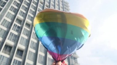 Kişi tarafından tutulan LGBTQ + gurur bayrağı renginde kalp şeklinde bir balon. Güneş ışınları eşitliği, cinsel özgürlüğü, cinsiyet saygısını ve dahil edilmeyi simgeliyor.