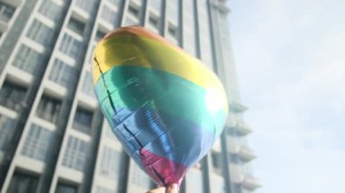 Kişi tarafından tutulan LGBTQ + gurur bayrağı renginde kalp şeklinde bir balon. Güneş ışınları eşitliği, cinsel özgürlüğü, cinsiyet saygısını ve dahil edilmeyi simgeliyor.