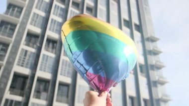 Kişi tarafından tutulan LGBTQ + gurur bayrağı renginde kalp şeklinde bir balon. Güneş ışınları eşitliği, cinsel özgürlüğü, cinsiyet saygısını ve dahil edilmeyi simgeliyor.