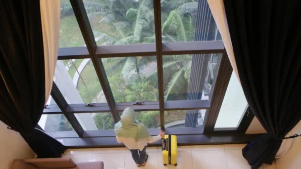 スーツケース付きの窓の近くに立っているムスリム観光女性のトップビュー — ストック動画