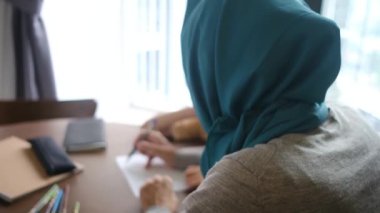 Müslüman bir kadın oğluna kağıt üzerinde yazmayı öğretiyor.