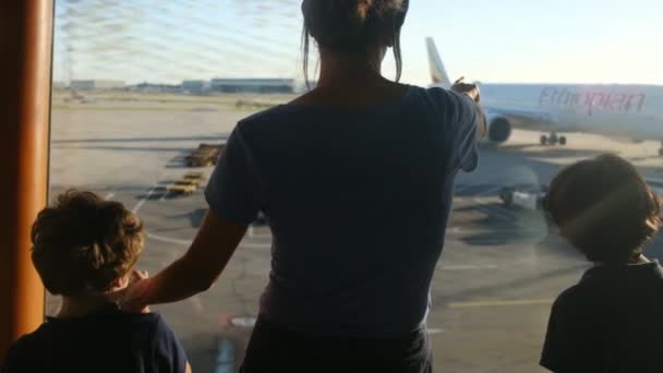 空港の窓からスーツケースを待っている息子と母親 飛行機を眺める — ストック動画