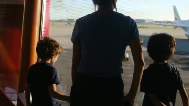 空港の窓からスーツケースを待っている息子と母親 飛行機を眺める — ストック動画