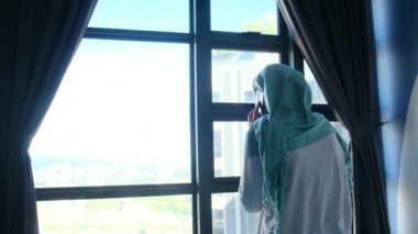 tesettürlü çekici müslüman kadın pencerenin yanında cep telefonu kullanıyor..