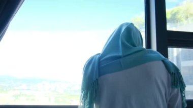 tesettürlü çekici müslüman kadın pencerenin yanında cep telefonu kullanıyor..