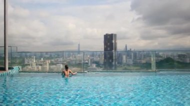 şehir silueti üzerinde sonsuz havuzda yüzen seyahat eden bir kadın. 