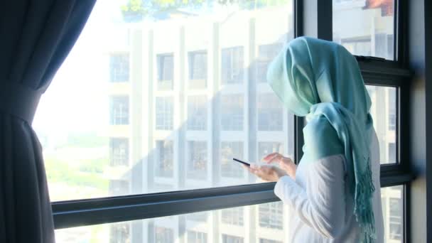 Tesettürlü Çekici Müslüman Kadın Pencerenin Yanında Cep Telefonu Kullanıyor — Stok video