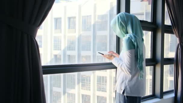 Tesettürlü Çekici Müslüman Kadın Pencerenin Yanında Cep Telefonu Kullanıyor — Stok video