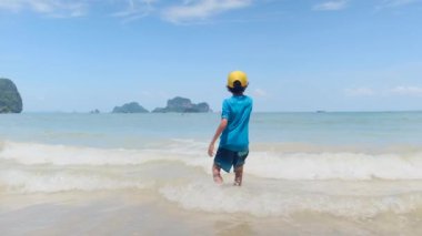 Küçük çocuk okyanustan hoşlanıyor, dalgalar halinde oynuyor, tatilde mutlu duygular yaşıyor.