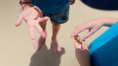 Küçük çocuklar sahilde satışta oynuyorlar. Bir çocuk parmağını şaklatıyor.