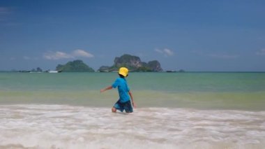 Küçük çocuk okyanustan hoşlanıyor, dalgalar halinde oynuyor, tatilde mutlu duygular yaşıyor.
