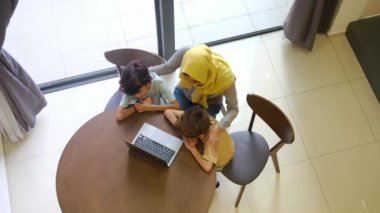 tesettürlü Müslüman anne ve çocukları, 5 ve 8, samimi bir Ramazan bayramı görüntüsü için bir dizüstü bilgisayarla bağlanıyorlar, teknolojiyle aralarındaki mesafeleri eşitliyorlar.