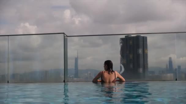 在城市天际线上方的天顶无限大池中游泳的女游客 — 图库视频影像