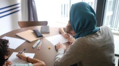 6 ve 8 yaşındaki çocuklarına evlerindeki okul görevlerinde rehberlik eden tesettürlü Müslüman bir anneye tanık olun.