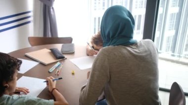 6 ve 8 yaşındaki çocuklarına evlerindeki okul görevlerinde rehberlik eden tesettürlü Müslüman bir anneye tanık olun.