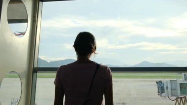 Solo gezgin havaalanı penceresinin yanında bavuluyla bekliyor, uçaklara bakıyor.