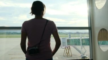 Solo gezgin havaalanı penceresinin yanında bavuluyla bekliyor, uçaklara bakıyor.
