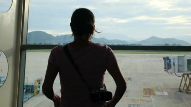 Solo gezgin havaalanı penceresinin yanında bavuluyla bekliyor, uçaklara bakıyor.