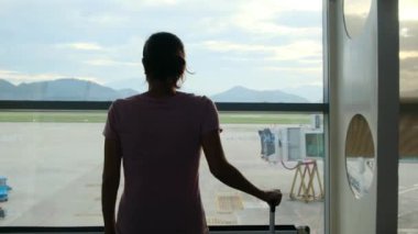 Solo gezgin havaalanı penceresinin yanında bavuluyla bekliyor, uçaklara bakıyor.