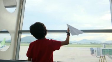 Çocuk havaalanında kağıt uçakla eğleniyor. 