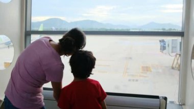Anne ve oğlu havaalanı penceresinde bekliyor, uçaklara bakıyor.