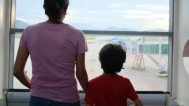 Anne ve oğlu havaalanı penceresinde bekliyor, uçaklara bakıyor.