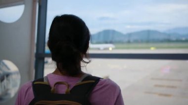 Solo gezgin havaalanı penceresinin yanında bavuluyla bekliyor, uçaklara bakıyor.