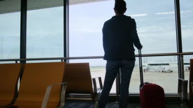 Solo gezgin havaalanı penceresinin yanında bavuluyla bekliyor, pistteki uçaklara bakıyor, macera beklentisini yakalıyor. Gezgin şehveti, havaalanı sahneleri, seyahat anları..