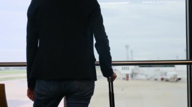 Solo gezgin havaalanı penceresinin yanında bavuluyla bekliyor, pistteki uçaklara bakıyor, macera beklentisini yakalıyor. Gezgin şehveti, havaalanı sahneleri, seyahat anları..