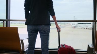 Solo gezgin havaalanı penceresinin yanında bavuluyla bekliyor, pistteki uçaklara bakıyor, macera beklentisini yakalıyor. Gezgin şehveti, havaalanı sahneleri, seyahat anları..
