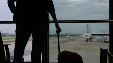 Solo gezgin havaalanı penceresinin yanında bavuluyla bekliyor, pistteki uçaklara bakıyor, macera beklentisini yakalıyor. Gezgin şehveti, havaalanı sahneleri, seyahat anları..